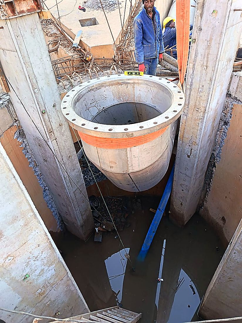 Large flanged steel pipe spool being lowered between reinforced concrete walls