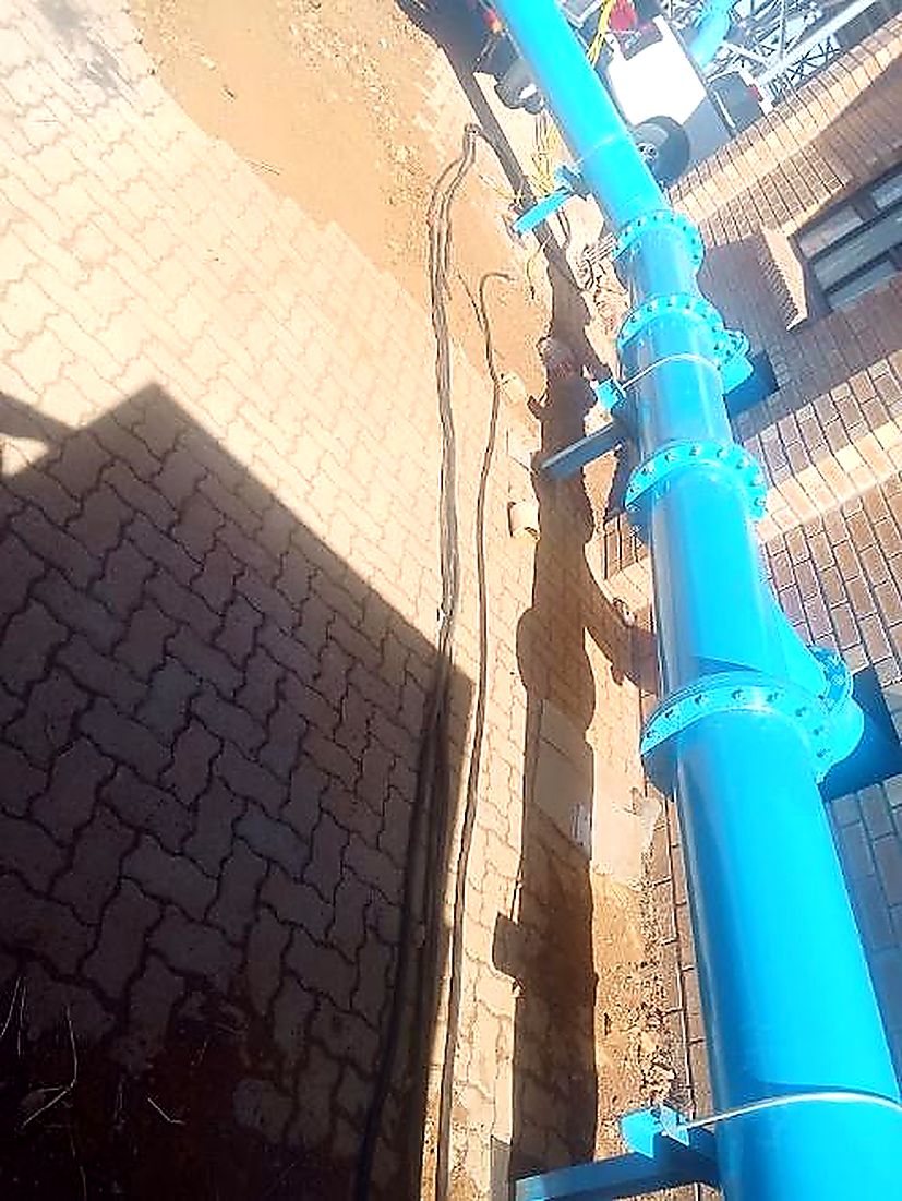 Large diameter blue rising main pipe fixed against pump house brickwork
